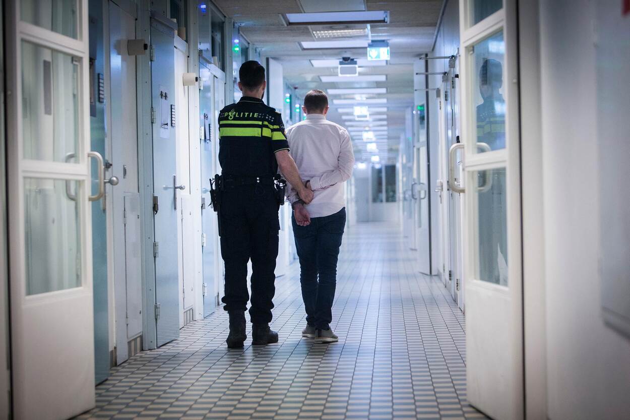 Politieagent met geboeide persoon in cellencomplex