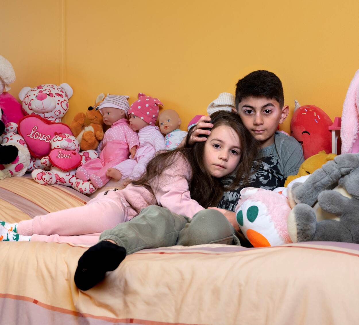 Twee Oekraïense kinderen tussen knuffels op een bed